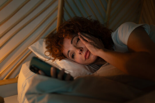 Woman suffering insomnia and anxiety scrolling phone in bed