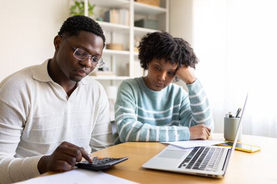 Stressed couple calculating domestic bills at home using calculator and laptop
