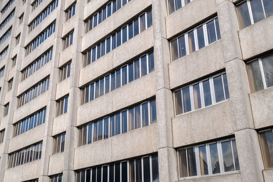 Exterior view of a tall disused and vacant office block featuring repetitive concrete windows and a gray facade during a cloudy daytime period
