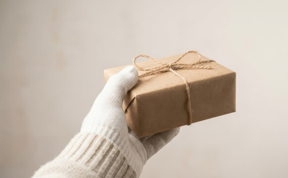 Gloved hand holding a small brown parcel wrapped with string for delivery and holiday gift giving
