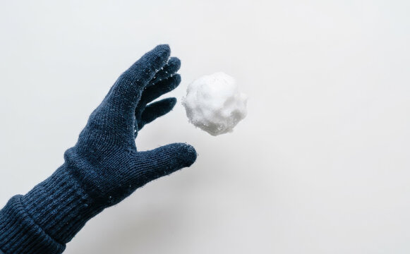 A person wearing a blue winter glove throwing a snowball against a plain white background