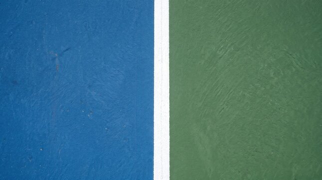 Tennis court surface featuring vibrant blue and green colors divided by a bright white line showing textured outdoor sports flooring