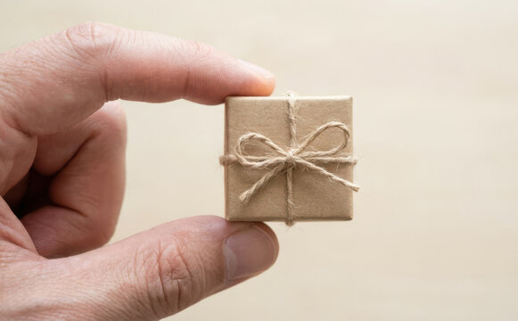 Tiny gift box held between fingers representing miniature present and surprise concept