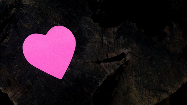 Pink paper heart placed on a dark natural rock surface, symbolizing love, romance, hope, and emotional strength with a creative minimalist composition.