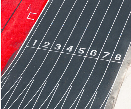 Black track surface with white lane markings and red starting blocks