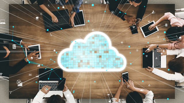 A teamwork-focused scene showing multiple professionals engaged with digital devices around a table, emphasizing cloud computing and data sharing in a modern office environment. Xenic