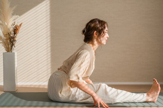 ヨガマットで脚を伸ばしてストレッチする女性。柔軟性と体を整えるナチュラルなヨガ習慣