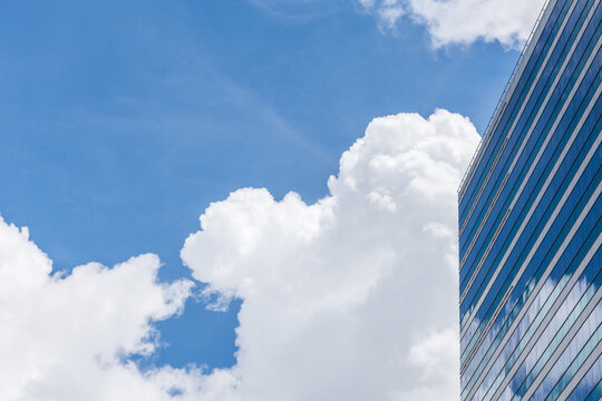 Modern glass office building beneath vivid blue sky large white clouds reflecting the facade generous copy space for business themes