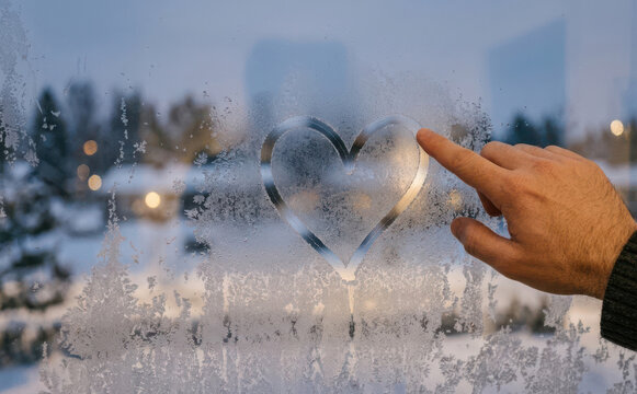 Drawing a heart on a frosted winter window with a finger, representing love, romance and cold weather affection