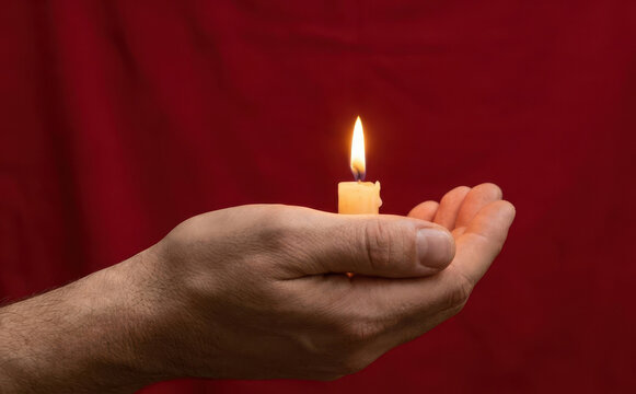 A man cupping his hands to hold a burning candle representing hope and remembrance