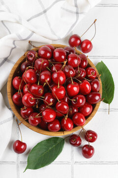 Top view of fresh ripe red sweet cherries in wooden bowl with green leaves on white tile textured background. Organic summer fruit, juicy berries, natural freshness, healthy eating, seasonal food