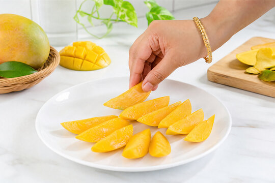 Hand taking fresh juicy sliced mango from white plate on kitchen table