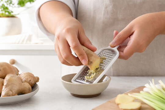 Hand grating fresh ginger on metal grater in bright kitchen