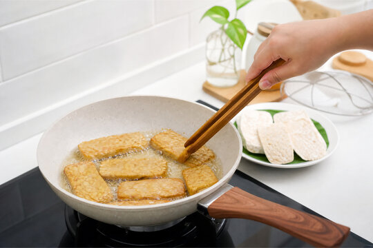 Frying tempeh slices in hot oil with wooden chopsticks in pan