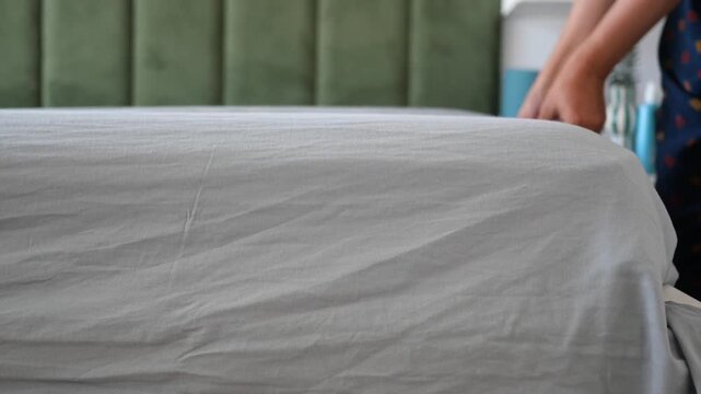 Unrecognized female arranging soft clean sheets on comfortable mattress in bedroom, closeup shot