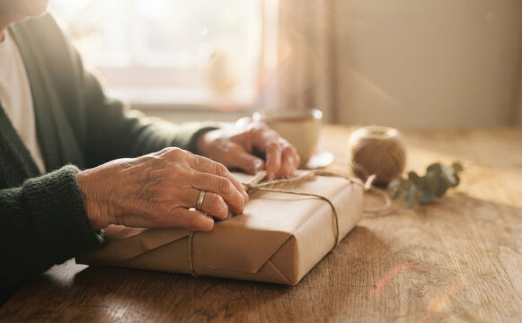 Elderly woman wrapping a parcel with brown paper and twine at home, conceptual image for mindful gift giving and sustainable packaging