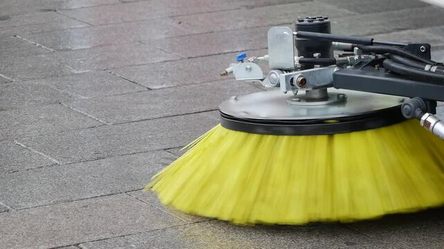 A close up view of a street sweeper brush cleaning a wet paved surface, showcasing dynamic motion and clean up process