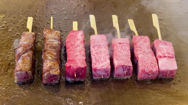 Raw cubes of wagyu beef on skewers being grilled on a hot plate.