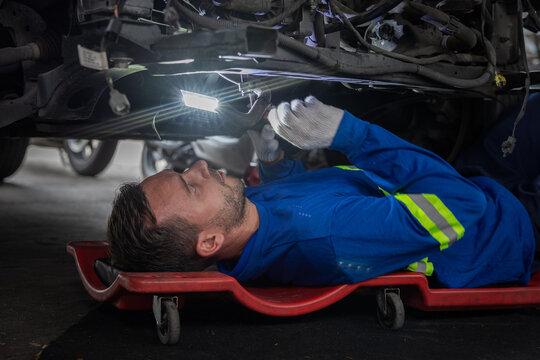 Man in blue coverall repairing vehicle underside in garage with EV underbody inspection light