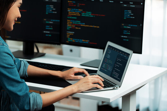 Smiling young Asian in IT developer creating with typing online information on laptop with coding program data of application, wearing jeans shirt. surrounded by safety analysis two screen. Stratagem.