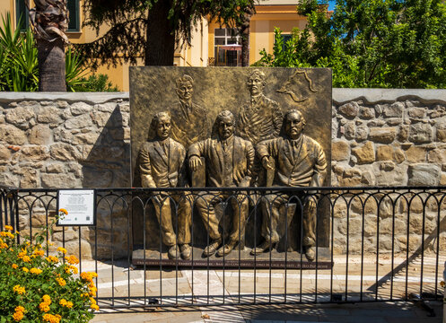 Capo d'Orlando, ME - IT - Sep 4, 2026 : A bronze relief monument dedicated to the founding fathers of autonomy of Capo d'Orlando in 1925 is mounted on a wall behind a black metal fence with flowers.