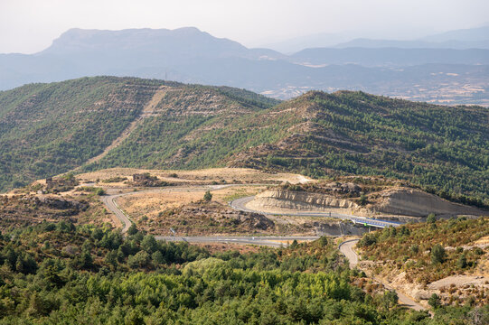 A view over the forested hills and a winding road in the foothills of the Spanish Pyrenees near Riglos in Aragon, Spain, a hazy summer landscape of green slopes and distant mountains.