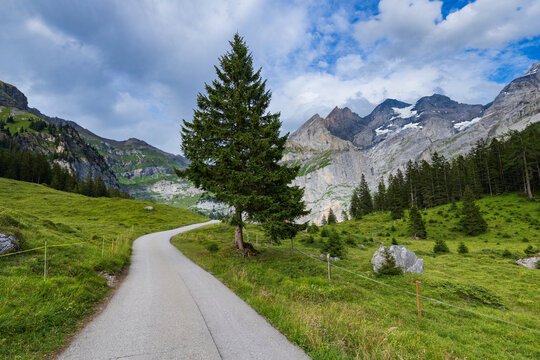 A paved path winds toward the mountains over Oeschinen Lake (Oeschinensee) near Kandersteg, Switzerland