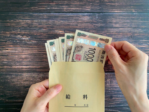木製テーブルで給料袋に入った紙幣を持つ女性の手元