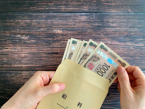 木製テーブルで給料袋に入った紙幣を持つ女性の手元