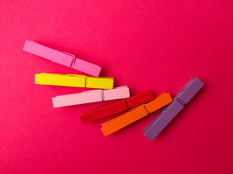 Six colorful wooden clothespins are lined up in a fanned diagonal row across a bright pink surface
