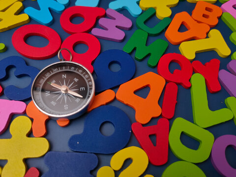 A silver navigational pocket compass rests over a field of scattered colorful wooden alphabet letters and numbers