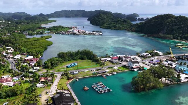 Aerial drone shot flying over a tropical island town and tranquil turquoise bay with lush green islands beyond.