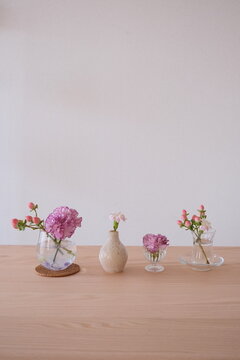お洒落な部屋の木目調テーブルに飾られたピンクの生け花と一輪挿しの写真、コピースペース有り