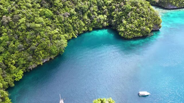 Cinematic aerial view of sailboat anchored in tropical lagoon with limestone islands and turquoise ocean.