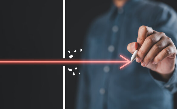 Business breakthrough and overcoming barriers concept with a hand pushing a glowing arrow through an obstacle for innovation, determination, problem solving, progress, success, leadership and growth.