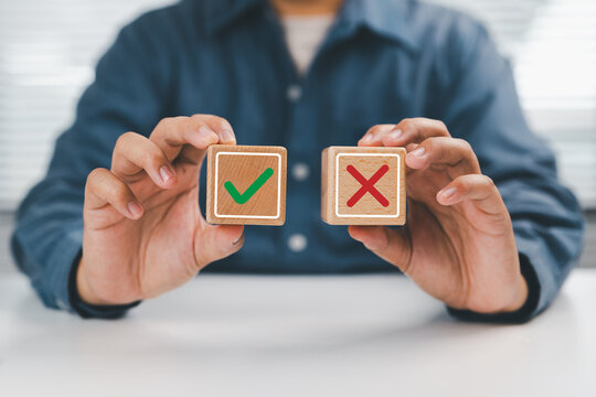Hands presenting red cross and green check blocks symbolize right or wrong choice of decision making with approval and rejection evaluation yes or no of business judgment concept.