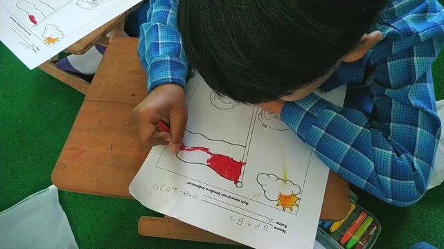 Child coloring Indonesian national flag drawing with red crayon on paper, closeup of hand education activity for kids