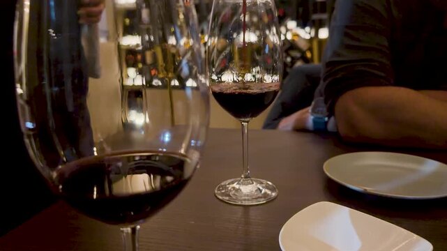 Close up of two glasses of red wine on a dark wooden table in restaurant setting.
