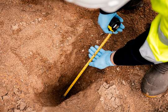 Environmental technician measuring soil pit depth during sample collection for soil quality analysis.