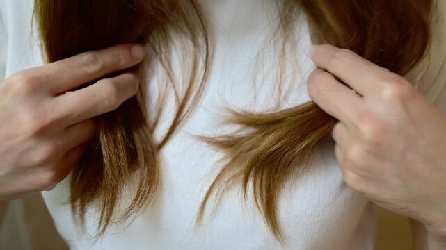 Asian woman holding and checking her damaged split ended hair. Hair damage is risk for further damage and breakage. It may also look dull or frizzy and be difficult to manage.