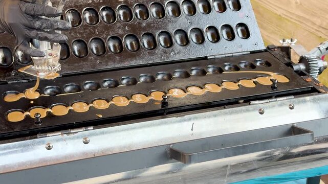 Street food vendor pouring sweet batter into specialized waffle maker machine with many oval molds.