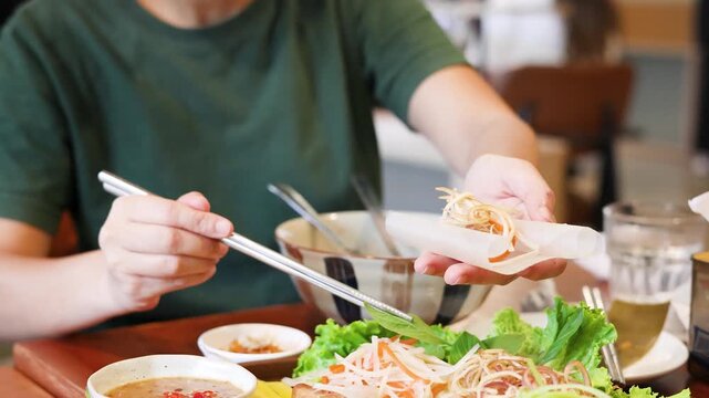 Woman hands preparing traditional Vietnamese fresh spring rolls with vegetables and pork in restaurant.