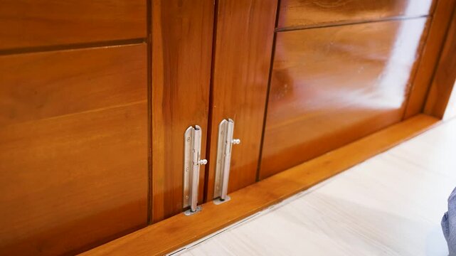 Man's hand opens a cabinet door latch with metal hardware on a wooden furniture.