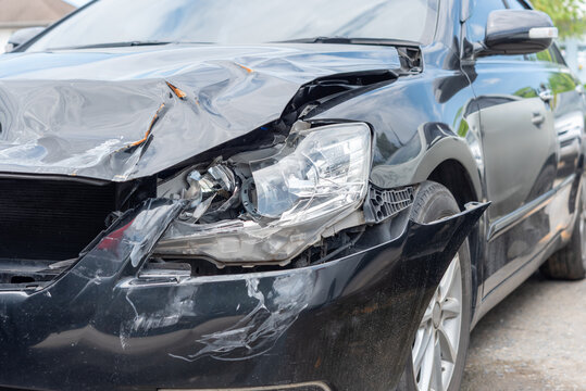 Black car severe front end collision damage broken headlight crushed hood detached bumper showing vehicle accident impact costly repair needs
