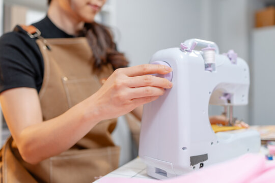 Professional fashion designer using a sewing machine in a modern studio while managing creative apparel production. Handmade craftsmanship, tailoring and small business workflow.