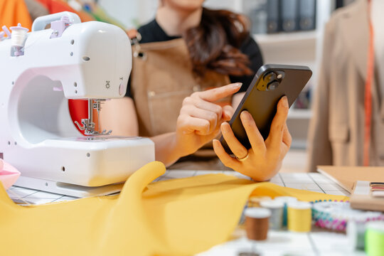 Professional fashion designer using a sewing machine in a modern studio while managing creative apparel production. Handmade craftsmanship, tailoring and small business workflow.