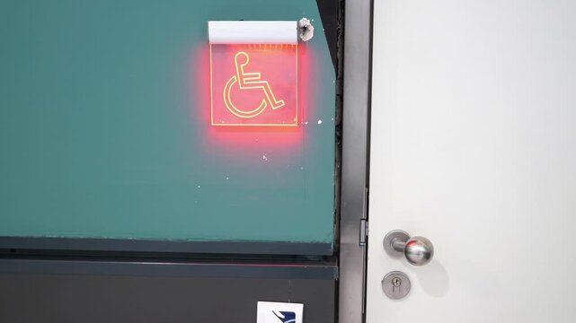 Accessible restroom sign with glowing red wheelchair symbol on wall next to white door