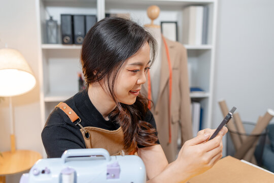 Professional fashion designer using a sewing machine in a modern studio while managing creative apparel production. Handmade craftsmanship, tailoring and small business workflow.