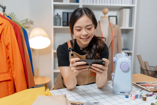 Professional fashion designer using a smartphone while managing a sewing studio and organizing tailoring supplies. Creative apparel production, small business and handmade craftsmanship.