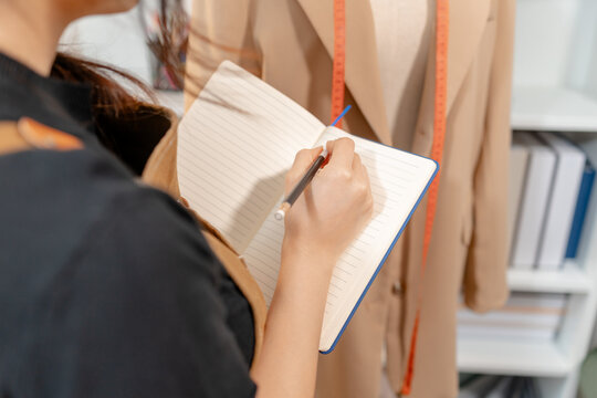 Fashion designer inspecting garment quality, measuring blazer fit and recording design details in a professional fashion studio. Apparel development, clothing quality control and textile craftsmanship